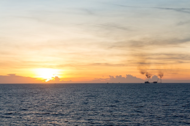 Sonnenaufgangansicht von der Küste mit dunkelblauer Meerwasser- und Öl- und Gasproduktionsplattform.