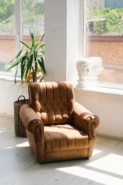 Foto sonnenbeleuchteter vintage-leder-sessel an einem großen fenster in einem hellen raum