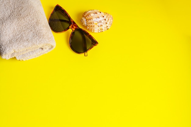 Sonnenbrille, Handtuch und Muschel auf gelbem Hintergrund, Kopierraum