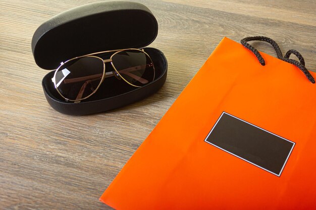 Sonnenbrille in einem Etui und orangefarbener Verpackung auf einem Holzhintergrund