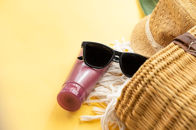 Sonnenbrille Sonnencreme und Stroh Strandtasche an gelber Wand