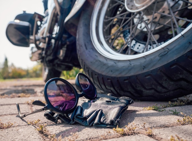 Sonnenbrillen und fingerlose Lederhandschuhe mit Schnürsenkeln in der Nähe des Rades eines Motorrads