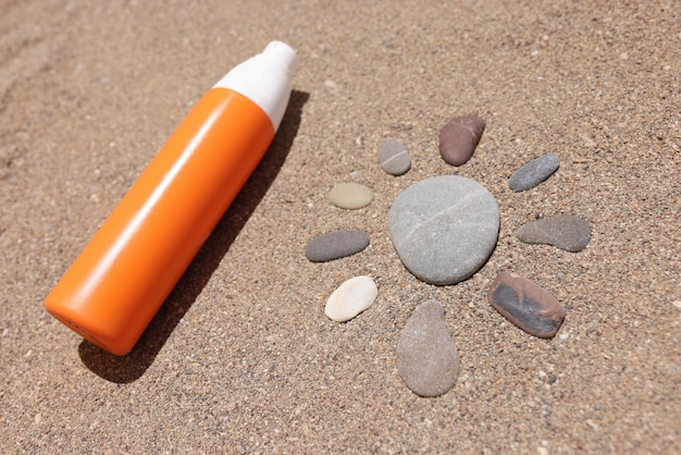 Sonnencreme liegt auf heißem Sand neben Sonnenfigur aus Steinen