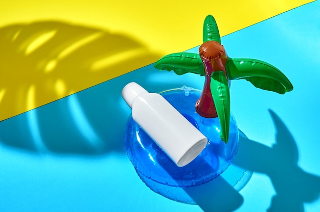 Sonnencremeflasche schwimmt auf aufblasbarem Kreis im Ozean und Palmblattschatten an einem Sandstrand. Attrappe, Lehrmodell, Simulation. Kreatives minimales Konzept.