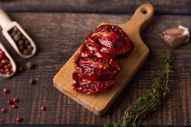 Sonnengetrocknete Tomaten in Olivenöl auf einem Minibrett mit Pfeffer, Knoblauch und Thymian im rustikalen Stil. Selektive Fokussierung in der Nähe