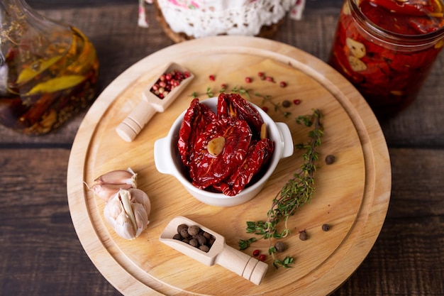 Sonnengetrocknete Tomaten in Olivenöl in einer weißen Schüssel mit Pfeffer, Knoblauch und Thymian auf einem Holzbrett Hausmannskost im rustikalen Stil Selektiver Fokus in der Nähe