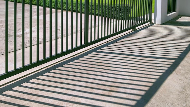 Sonnenlicht und Schatten auf der Oberfläche des automatischen Schiebezauntors aus Metall vor dem modernen Haus