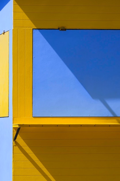 Sonnenlicht und Schatten auf der Oberfläche des gelben und blauen Kaffeestraßenkiosks im vertikalen Rahmen