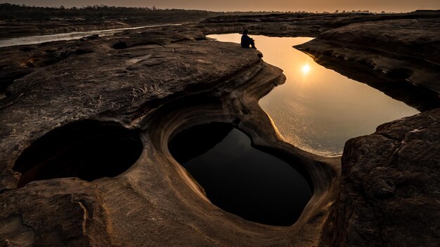 Sonnenlichtreflexion auf der Wasseroberfläche in der Morgenszene und Silhouette kleines junges Mädchen, das trauriges und einsames Konzept im Grand Canyon Sam Phan Bok Ubon Ratchathani Thailand sitzt