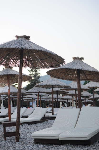 Sonnenliegen mit Strohschirmen am Kiesstrand Abends keine Menschen