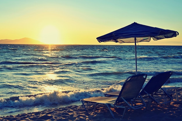 Sonnenliegen und Sonnenschirm am Strand bei Sonnenuntergang am Meer Schönes Konzept für Ferien, Sommerferien und Reisen