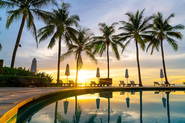 Sonnenschirm und Stuhl rund um den Swimmingpool im Hotelresort mit Sonnenaufgang am Morgen - Urlaubs- und Urlaubskonzept