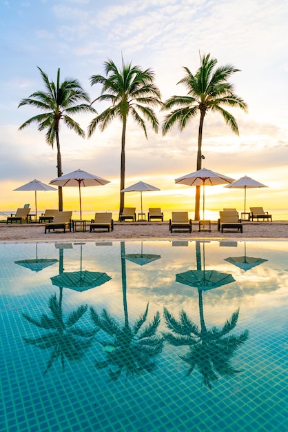Sonnenschirm und Stuhl um Schwimmbad im Hotelresort mit Sonnenaufgang am Morgen - Urlaub und Ferienkonzept