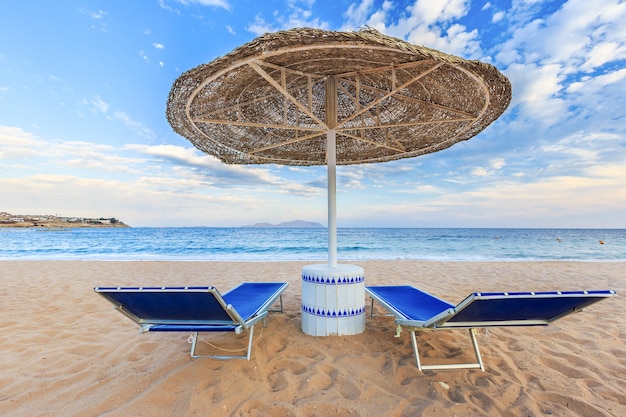 Sonnenschirm und zwei leere Liegestühle am Ufersandstrand