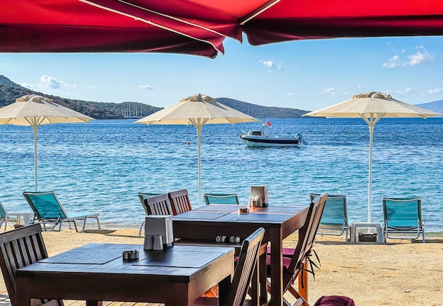 Sonnenschirme, Liegestühle, Tische und Stühle am Ufer der blauen Meeresbucht Sommerurlaubskonzept