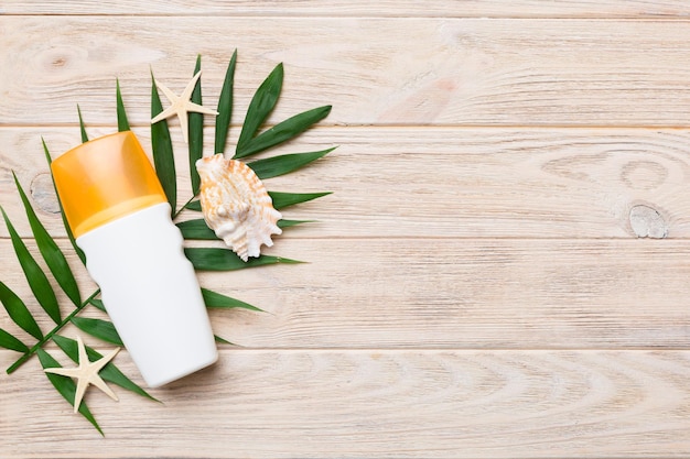 Sonnenschutz-Sprühflasche Flasche mit Sonnenschutzcreme und Muscheln mit tropischem grünem Blatt auf farbigem Hintergrund Draufsicht