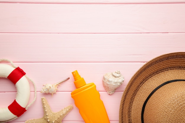Sonnenschutzflasche mit Hut, Brille und anderem Zubehör auf rosa Hintergrund.