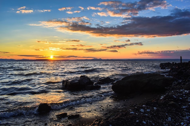 Sonnenuntergang am Meer, auf das die Wellen viele Algen und Muscheln geworfen haben. Sonnenlicht wird in der reflektiert