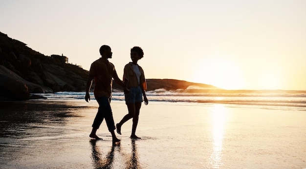 Sonnenuntergang am Strand und Silhouette eines Paares, das Händchen haltend auf dem Sand spaziert und eine romantische Zeit zusammen genießt
