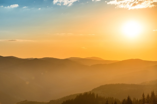 Sonnenuntergang in den Bergen mit Wald und großer strahlender Sonne am dramatischen Himmel