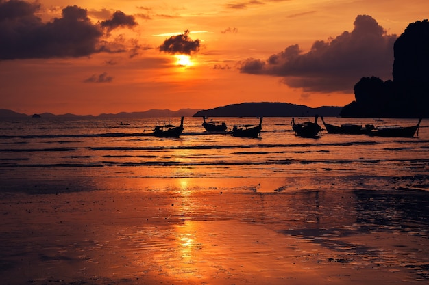 Sonnenuntergang mit dramatischem Himmel über dem Meeresstrand mit traditionellen Longtail-Booten