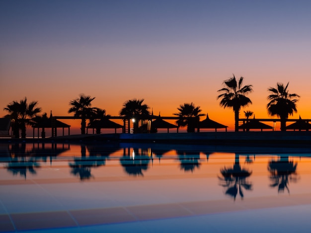 Sonnenuntergang mit silhuettes Palme und Reflexion im Swimmingpool