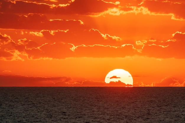 Sonnenuntergang oder Sonnenaufgang im Hintergrund mit orangefarbenem Himmel und Sonnenscheibe, die über dem Meereshorizont aufgeht