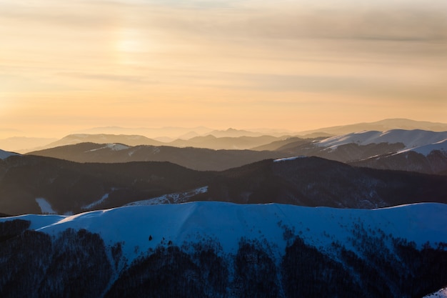 Sonnenuntergang über den mit Schnee bedeckten Berggipfeln im klaren Wintertag oder in der Dämmerung