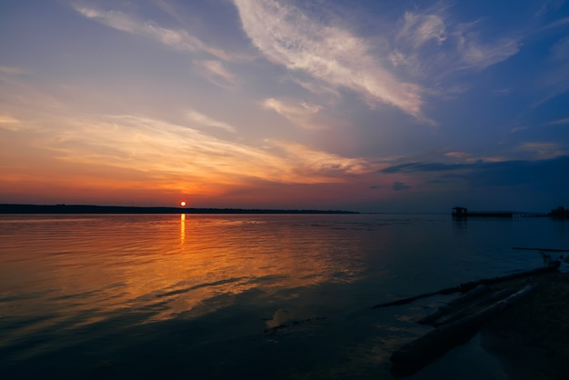 Sonnenuntergang über Fluss und schönem Himmel am Sommerabend und am Schattenbild des Piers