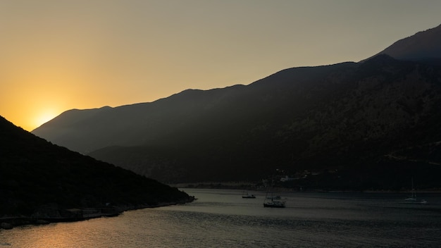 Sonnenunterganglandschaft eines Strandes mit kontrastierenden Bergen im Hintergrund und Booten, die in der Türkei segeln