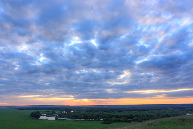 Sonnenunterganglandschaft mit wunderbarem goldenem und rosa Himmel, erstaunlichen purpurroten Wolken am Abend während des Sonnenuntergangs über grünen Feldern und einem Wicklungsfluß