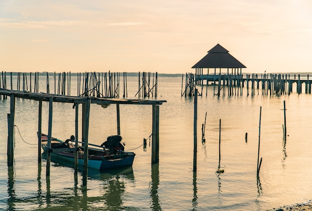 Sonnenuntergangshimmel über Meer am Morgen und öffentlicher Pavillon mit Fußgängerbrücke und selektiv auf Fischerboot Vordergrund
