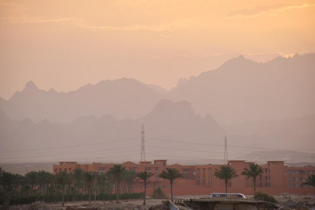 Sonnenuntergangslandschaft mit abgelegenem Hotelkomplex vor dunklen Berggipfeln in der ägyptischen Wüste