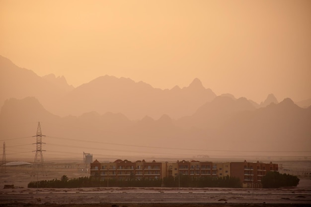 Sonnenuntergangslandschaft mit abgelegenem Hotelkomplex vor dunklen Berggipfeln in der ägyptischen Wüste