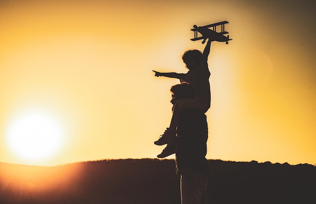 Sonnenuntergangssilhouette von Kind und Vater, die Kinderpilotenflieger spielen, und Vater träumt davon, glücklichen Jungen zu reisen ...