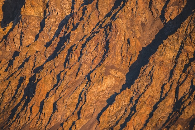 Sonniger Naturhintergrund von Rocky Mountains im Sonnenlicht. Lebendige natürliche Gebirgsbeschaffenheit der großen rauen Felsen. Voller Rahmen der hellen riesigen schroffen Oberfläche. Rocky Mountain Nahaufnahme. Ebene der glänzenden Felsen auf Sonnenuntergang.