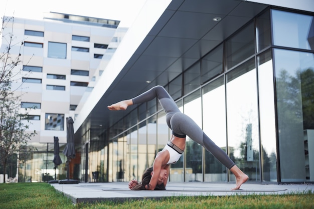 Sonniger Sommermorgen. Junge athletische Frau, die Handstand auf Stadtparkstraße unter modernen städtischen Gebäuden tut. Übung im Freien gesunden Lebensstil.