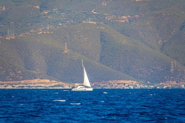 Sonniger Sommertag. Hohe Hügel am Ufer. Weiße Yacht segelt mit Segel