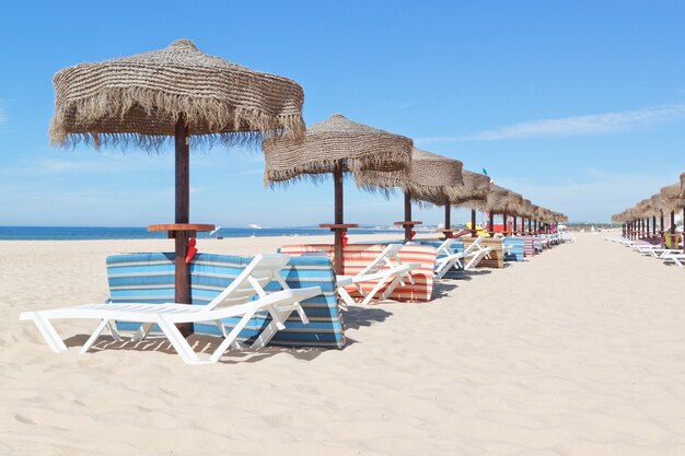 Sonniger Strand in Portugal mit einer Reihe von Sonnenschirmen in der Nähe des Meeres. Sommer.