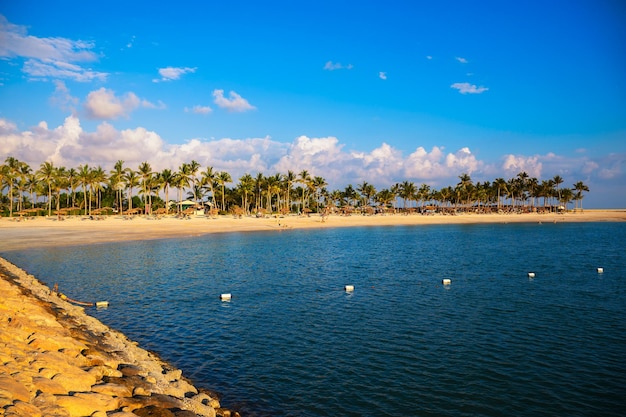 Sonniger Strand mit Palmenschirmen und Touristen in Salalah Oman