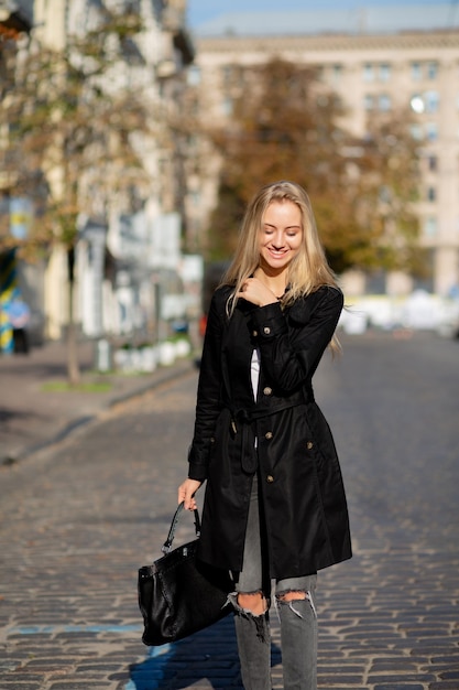 Sonniges Frühlingsporträt eines fröhlichen blonden Modells, das warmes Wetter genießt und die Straße entlang geht