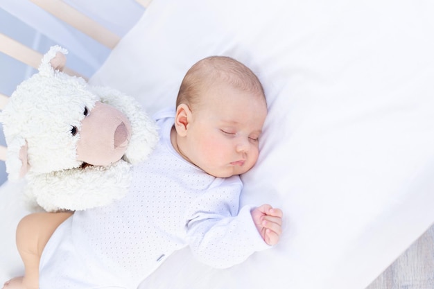 Sono saudável de um bebê recém-nascido em um berço no quarto com um urso de pelúcia em uma cama de algodão