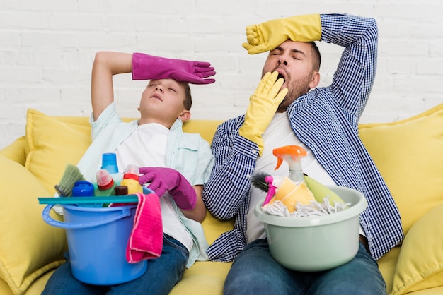 Sonolento pai e filho descansando no sofá depois de limpar a casa