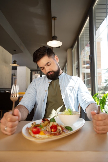Foto soñoliento y hambriento. hombre barbudo soñoliento sosteniendo un cuchillo y un tenedor mientras quiere comer en el restaurante