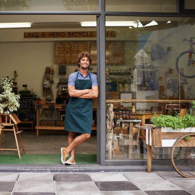 Sonríe a la cafetería y piensa con el hombre como propietario de una pequeña empresa en la puerta de entrada. Persona emprendedora feliz como gerente de barista o mesero en un restaurante para una idea de bienvenida, orgullo profesional y objetivos de inicio.