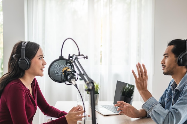 Sonríe a dos jóvenes asiáticas, anfitriones de radio con auriculares, micrófono mientras habla, conversa, graba podcast en la transmisión en el estudio juntos. Tecnología para hacer un concepto de grabación de audio.