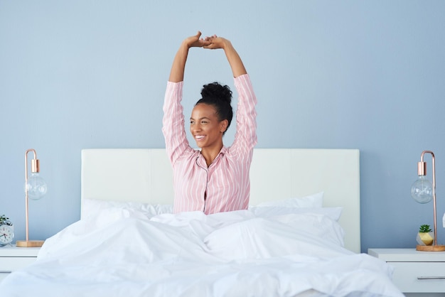 Sonríe mujer negra y estirando los brazos en la cama para la mañana tranquila buen sueño y listo para comenzar el día en casa chica africana colchón y feliz estiramiento para despertar sueño pacífico y relajarse en el dormitorio