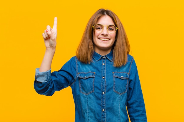 sonriendo alegre y alegremente, apuntando hacia arriba con una mano para copiar espacio