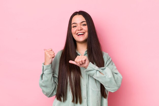 Sonriendo alegre y casualmente señalando el espacio de copia en el costado sintiéndose feliz y satisfecho