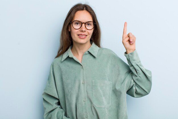 Sonriendo alegremente y felizmente apuntando hacia arriba con una mano para copiar espacio